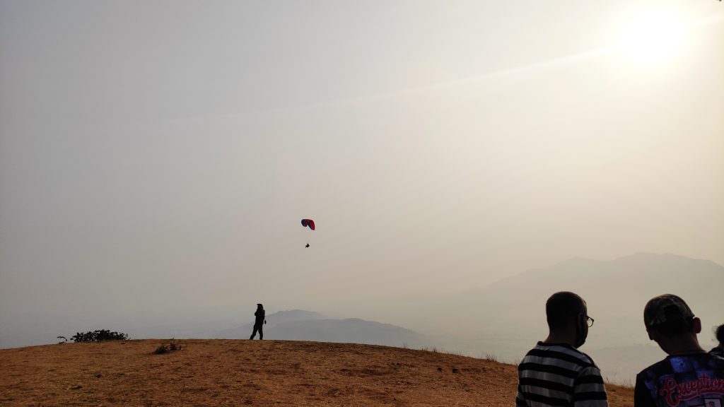A couple of people standing on top of a hill flying a kite