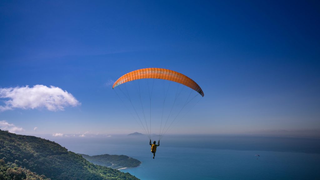 A paraglider soaring over the scenic landscapes of Kamshet, showcasing stunning blue skies, lush green hills, and serene waters, perfect for adventure seekers interested in Kamshet paragliding.
