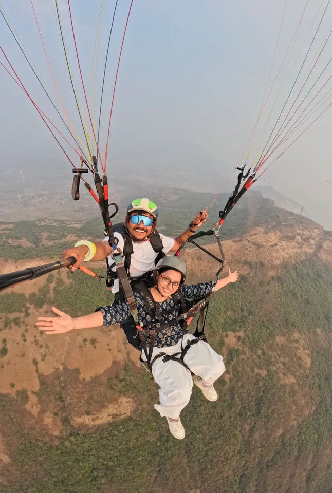 A smiling guest flying tandem with a pilot above the hillside