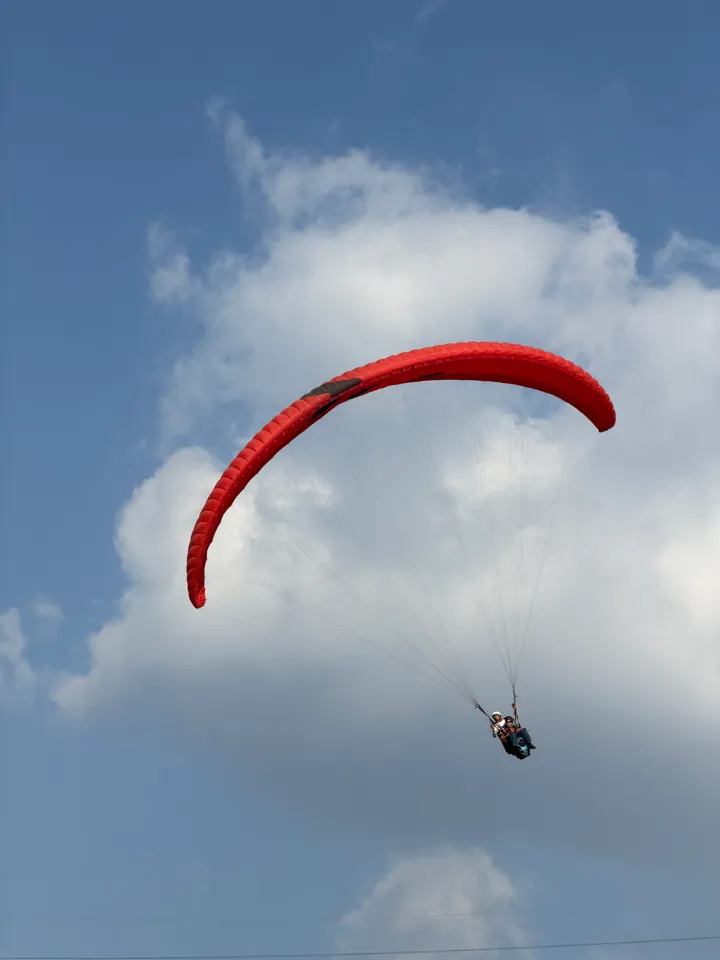 Tandem flyers suspended below a red paraglider in an open blue sky