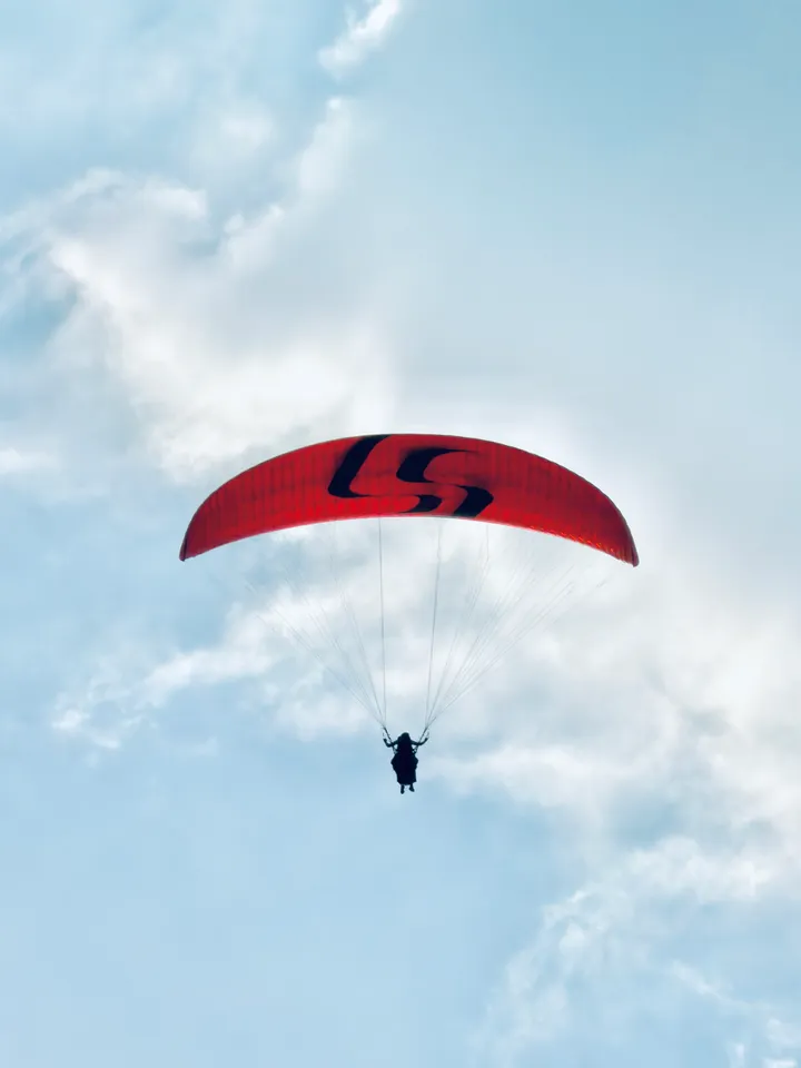 A red paraglider and tandem flyers against blue sky and white clouds