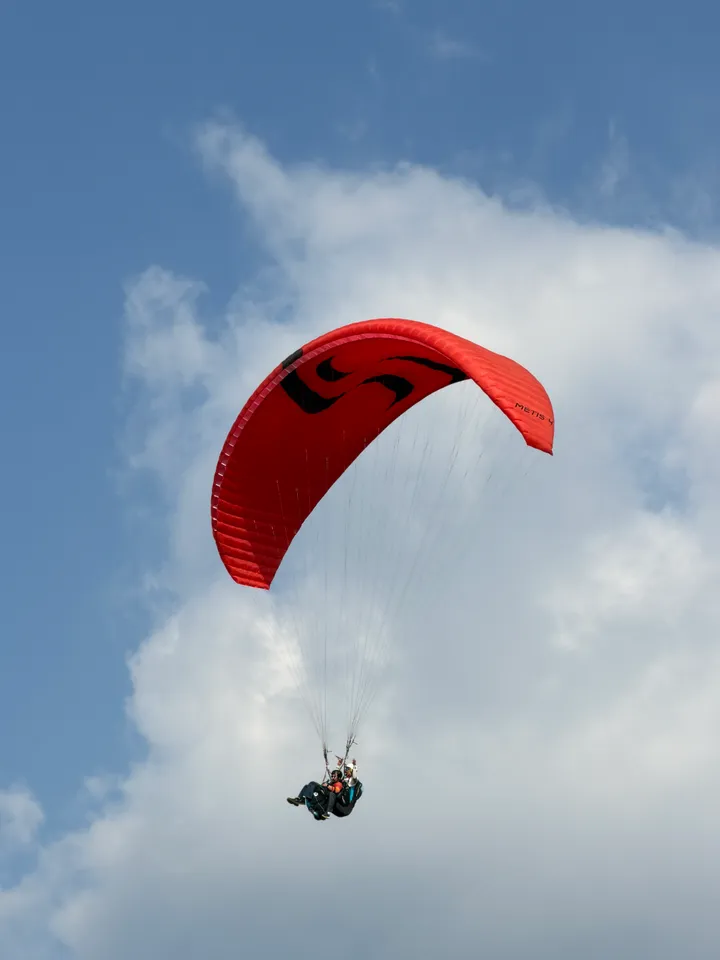 A red paraglider banking against a bright sky with clouds