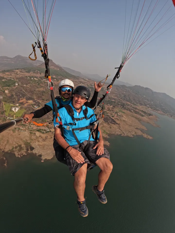 A guest and pilot paragliding above a lake and rugged hills