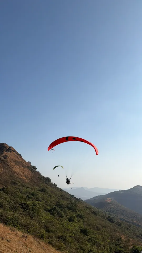 A red paraglider flying beside a green hillside above the valley